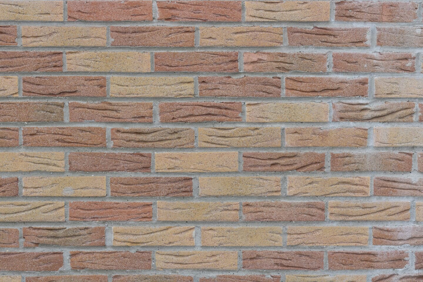 Getextureerde geel-rode bakstenen buitenmuur met lichte atmosferische vervuiling en aanslag op de stenen en het voegwerk.