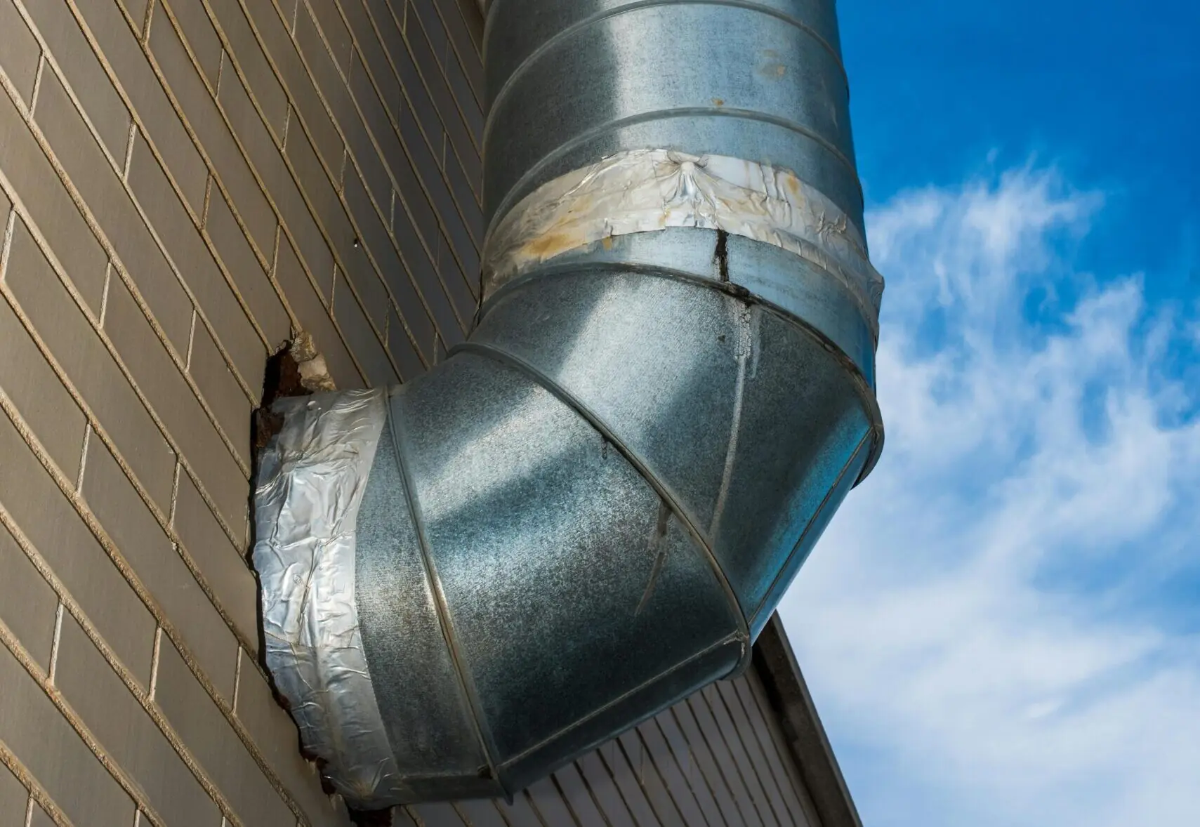 Ventilatiepijp die uit een gebouw steekt en het dak op gaat.